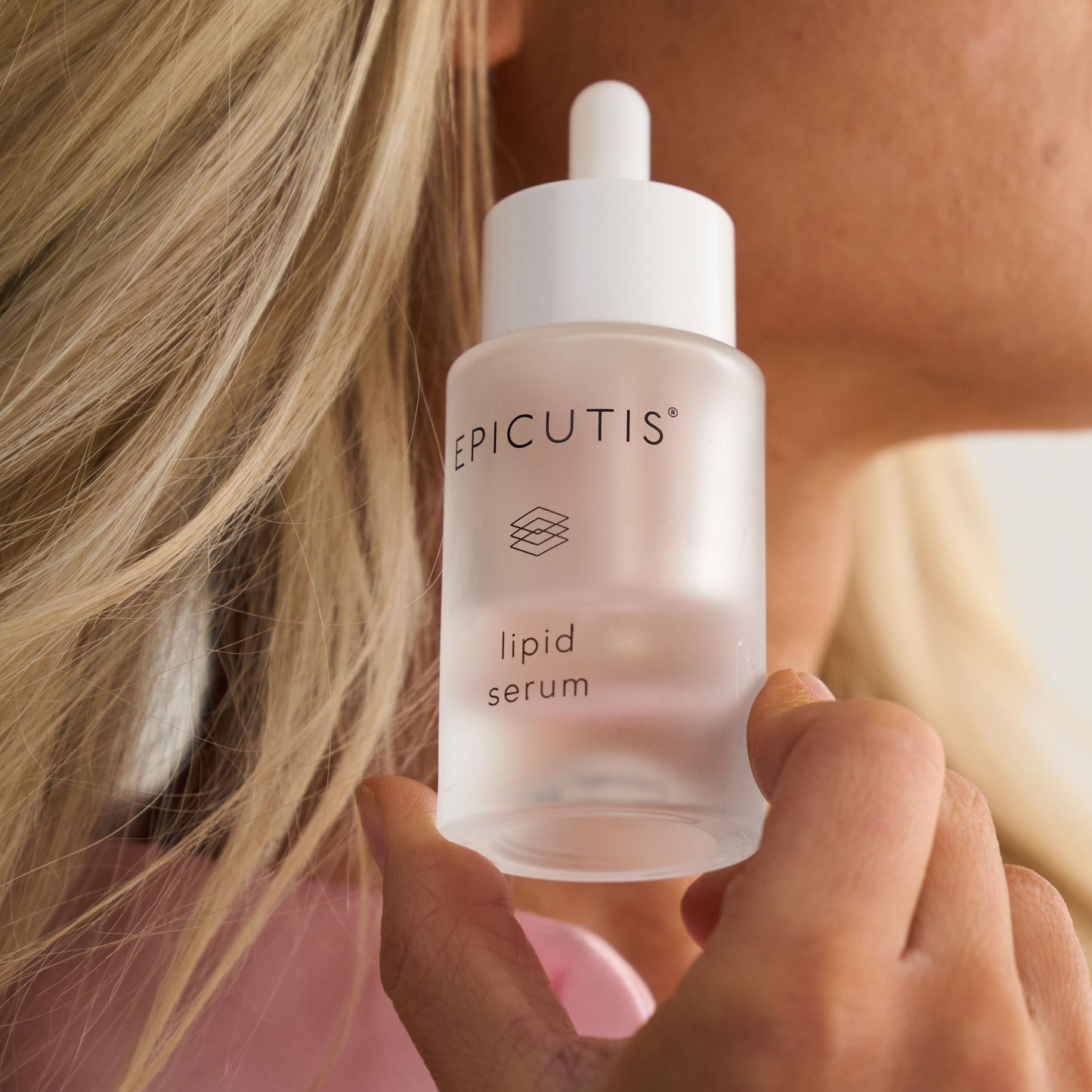 Woman holding a bottle of Epicutis lipid serum against a neutral background