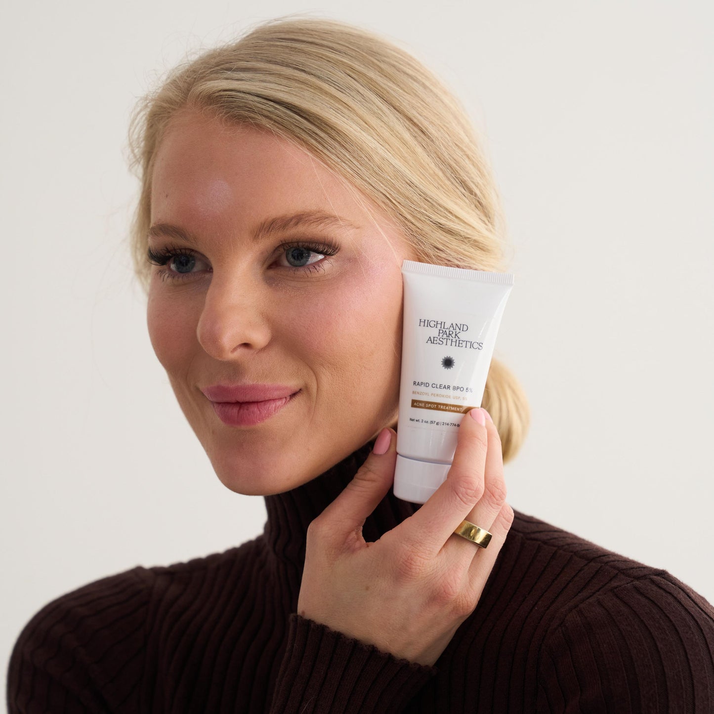 Woman holding a skincare product against a plain background